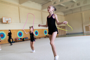 Girl gymnast jumping with rope on training in gym with other trainees