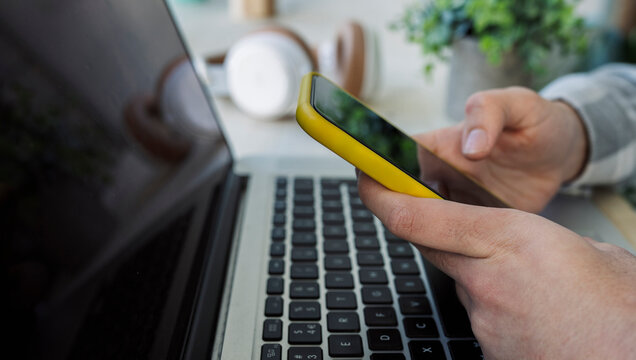 Unrecognizable person browsing smartphone near laptop