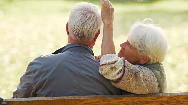 An Elderly Couple Sitting On The Bench In The Park. Woman Leaning Her Head On Man's Shoulder And Caressing His Hair. High Quality 4k Footage