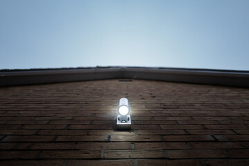Vertical focus of a PIR LED security light seen lit on the outside of a new home. Dew and a cobweb can be seen on the lights metal housing.