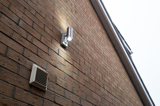 Exterior up and down PIR security light seen on an exterior wall of a new home. A steam extractor fan is in the lower left.