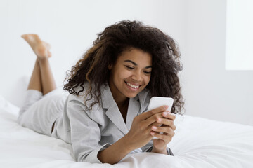African american woman using smartphone, lying on bed