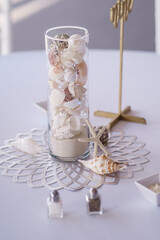 A transparent vase filled with white seashells on white background Close up Wedding decorations Wedding venue decor Reception details White table background Sea theme wedding decoration
