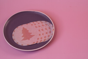 Round pieces of sausage with Christmas tree on it on pink background.