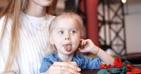 Disobedient child. The little girl litters the cafe, and her mother cleans up after her. Young family