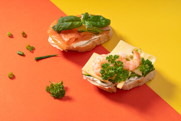 Little baguette sandwiches on vibrant yellow and orange background decorated with greens