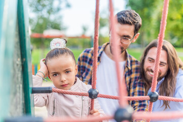 Girl in playground with her parents looking at camera unhappy.