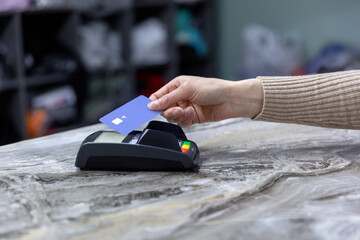Hand of customer paying with contactless credit card with NFC technology. Bartender with a credit card reader machine at bar counter with female holding credit card. Focus on hands.