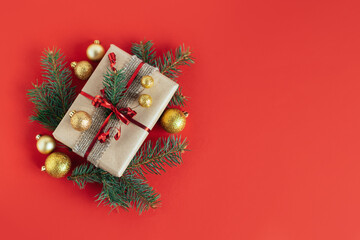 Craft gift box with spruce branch and christmas ornaments on a red background.