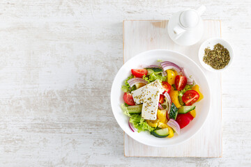 Fresh summer vegetable salad with lettuce, tomato, cucumber, bell pepper, onion and feta cheese, dressed with olive oil. Top view