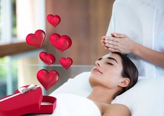 Heart icons over a heart shaped gift box against woman receiving a head massage at a spa