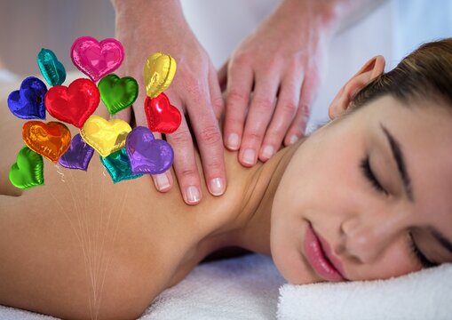 Composite image of bunch of colorful heart shaped foil balloons against woman receiving a massage