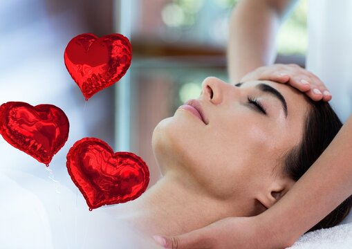 Composite image of red heart shaped foil balloons against woman receiving beauty face treatment
