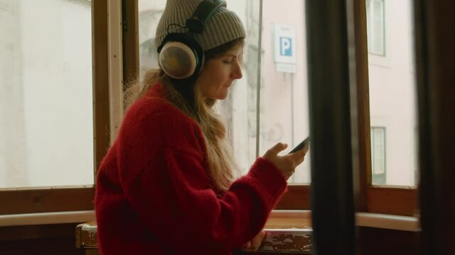 Young beautiful woman in tram or bus look out of rear window. Cinematic authentic shot of millennial youth use public transport, listen to music and scroll through phone. Concept travel solo