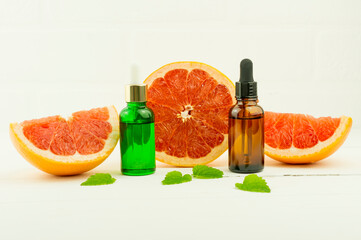 vitamin C serum, a bottle of organic grapefruit essential oil on a white background with grapefruit slices and lemon balm leaves