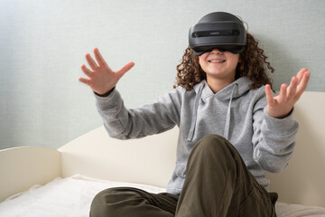 Teen girl wearing Virtual Reality headset is experiencing amazement VR sitting on bed home.