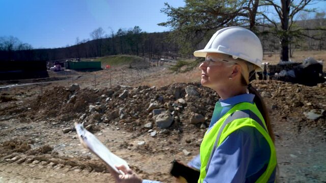 Extreme closeup of woman engineer architect wearing yellow vest and hard hat, walking by gravel and dirt piles on a contruction site.