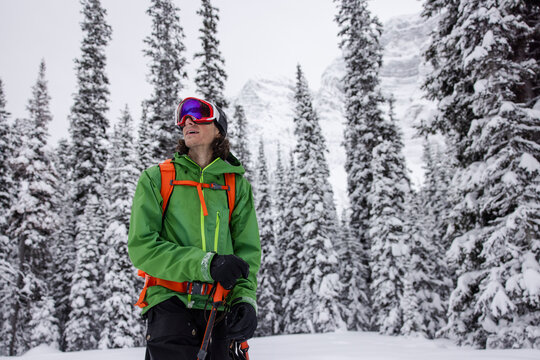 Curious Male Skier Looking Up Below Snowy Trees And Mountain