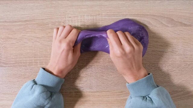Playing with slime, stretching the gooey substance for fun and stress relief. Close up and top view of female hand holding purple shining slime and squeezing it. 4K video