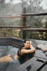 Young woman in a bikini bathing in japanese style bath outdoors while raining. Mountain resort spa and entertainment