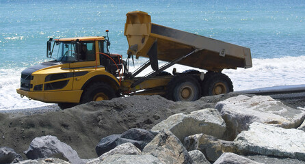   Industrial dumper trucks working on a construction in Genova city beach - Digging and moving sand...