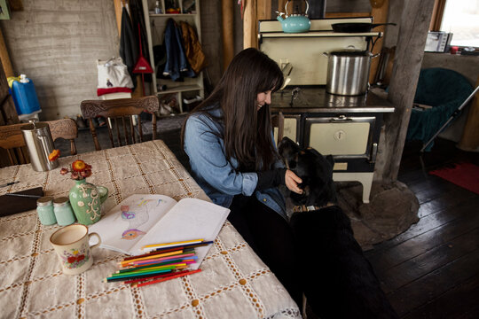 Woman with coloring book stroking dog in kitchen
