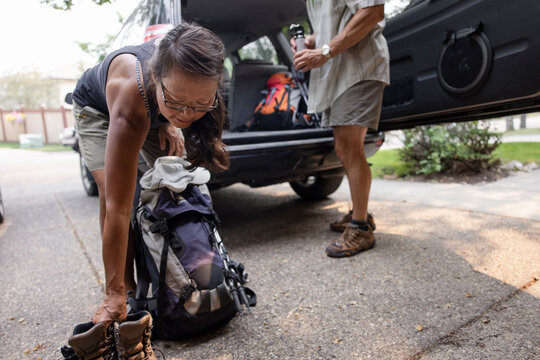 Woman loading hiking boots and backpack into car in driveway