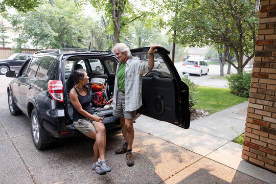 Senior Couple With Hiking Gear Talking At Back Of Car In Driveway