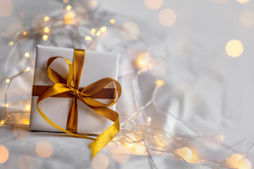 Gift box wrapped in white paper with golden ribbon bow on a soft background with yellow bokeh of...
