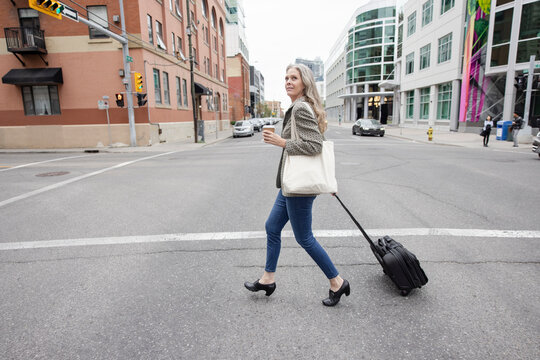 Businesswoman pulling wheeled luggage, crossing street