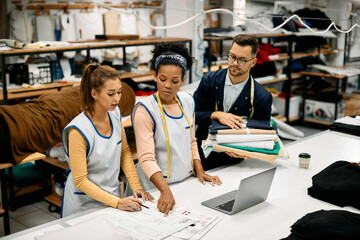 African American seamstress and her Caucasian co-workers analyzing while working on new project in...