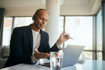 Happy African American businessman having conference call over laptop while working in office.