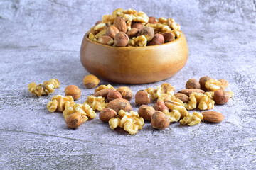 Assortment of nuts, walnuts, hazelnut and almond on a stone base and in a wooden bowl.