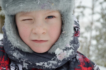 A large portrait of a funny child, a boy winking with one eye in a hat in winter