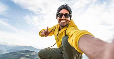 Young hiker man taking selfie portrait on the top of mountain - Happy guy smiling at camera - Hiking and climbing cliff - obrazy, fototapety, plakaty