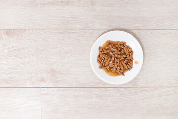 a plate with wet cat food on the background of a light wooden floor. High quality photo