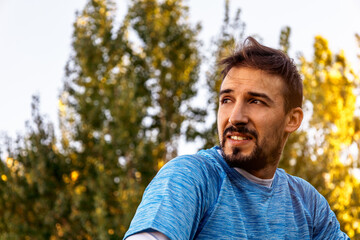 close-up portrait of smiling white man with blue shirt in a forest, sun beam in the back