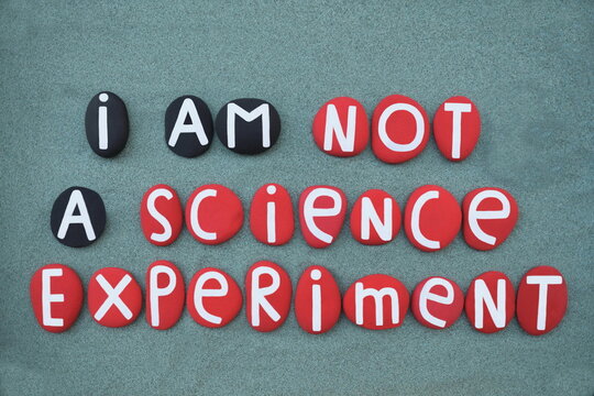I am not a science experiment, social slogan composed with red and black colored stone letters over green sand