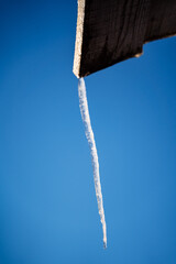 A thin icicle hangs from the roof. Frozen water in winter. Winter phenomena of nature. Sharp icicle. Minimalistic shot
