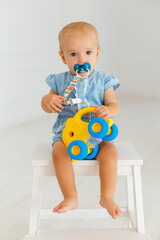 Сute baby girl in blue jeans holding yellow elephant. Little toddler sitting on the white wooden chair with pacifier in mouth. Portrait of one year child