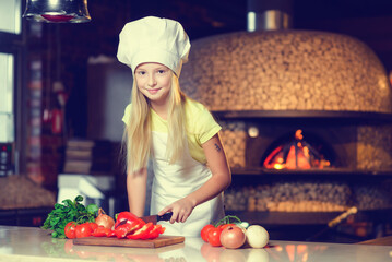 A little girl dressed as a cook prepares breakfast from vegetables.