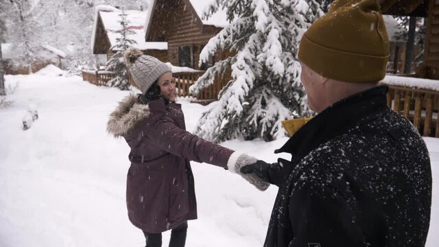 Couple Holding Hands Walking In Snow Outside Winter Cabins