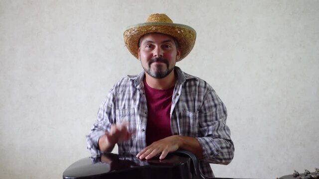 The man hits the guitar with his hands. On his head is a straw hat. Checkered shirt. Country style. Musician. Rock music. Portrait of a 40-year-old man.