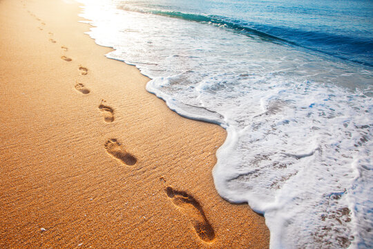 beach, wave and footprints at sunset time