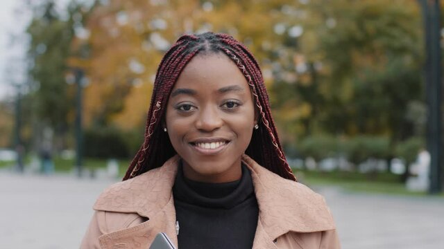 Closeup headshot attractive smiling millennial African American lady successful businesswoman or female student with laptop walking downtown in autumn clothing. Happy young woman looking at camera 
