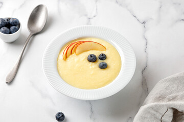 Сorn yellow porridge with fruits blueberry and apple on marble background with spoon