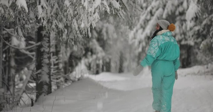 Young woman winter portrait in full height outdoors. Adorable young adult girl in ski suit walking in the mountain snowy forest.
