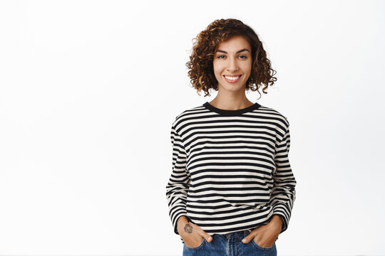 Stylish modern middle eastern girl with curly short hair, posing in casual clothes against white backgrund, smiling and looking confident