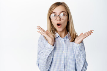 Surprised small girl, teenager in glasses looking amazed, standing over white background