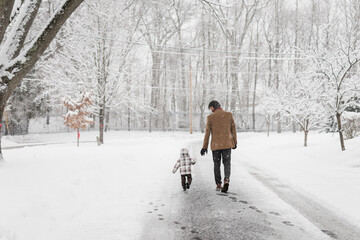 Dad and toddler walk down street on a snowy day in a neighborhood